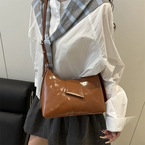 Glossy caramel brown leather underarm bag with gold clasp shown on a model