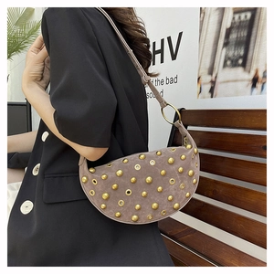 Detail of studded crescent crossbody bag in taupe suede shown on a model's shoulder