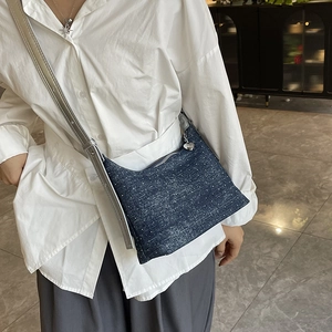 Polka dot denim crossbody dumpling bag with heart pendant worn by model in white shirt