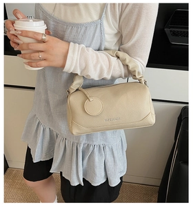 Detail of beige lychee pattern leather Boston bag with pleated handle and metal logo