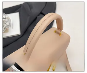 Primer plano de un bolso beige con asa semicircular reforzada y cierres metálicos dorados