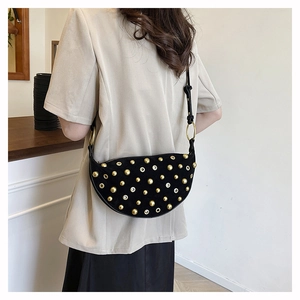 Detail of black suede saddle bag with gold stud rivets and eyelets on model's shoulder