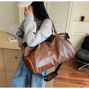 Detail view of a vintage brown leather travel bag featuring reinforced handles and shoulder strap