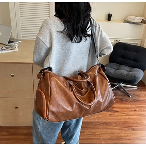 Detailed view of the large brown leather duffel bag with double handles and shoulder strap