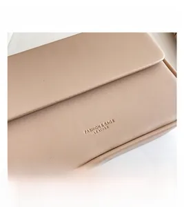 Gros plan sur la texture cuir grainé beige et le logo embossé sur le sac à rabat