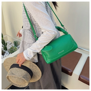 Street style view of a green leather Boston bag with a top handle and shoulder strap