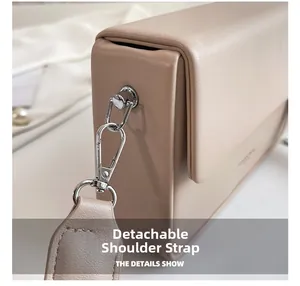 Détail de la bandoulière amovible avec boucle argentée sur un sac boîte en cuir beige