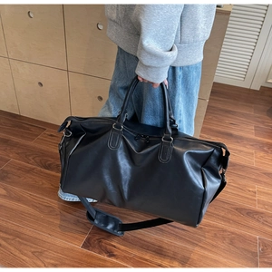 Close-up of a black leather travel bag with adjustable shoulder strap and sturdy handles