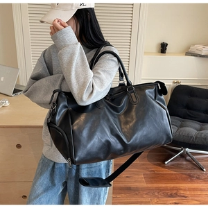 Detail of a large black faux leather travel bag with adjustable strap and matte texture