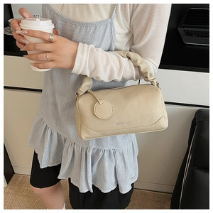 Detail of beige Boston bag with pleated handle and pebbled texture leather on model