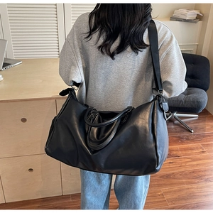 Rear view of model wearing a black large capacity PU leather duffel bag with shoulder strap