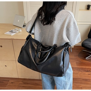 Close-up of black leather weekend bag with thick handles and canvas shoulder strap