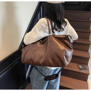 Man carrying large dark brown leather travel bag on stairs showing shoulder strap detail