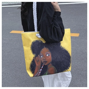 Outdoor street view of a yellow canvas tote bag with black girl print and rope straps
