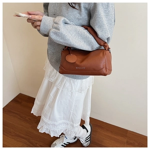 Close-up of brown leather Boston bag featuring a stylish knotted handle and metal logo