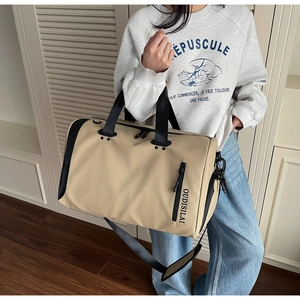 Bolsa de viaje grande en caqui con correa de hombro y logo en un entorno doméstico