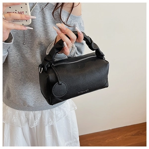 Detailed close-up of black litchi grain leather texture and twisted handle on Boston bag