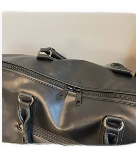 Detail view of the smooth dual zipper closure and leather texture on black travel bag