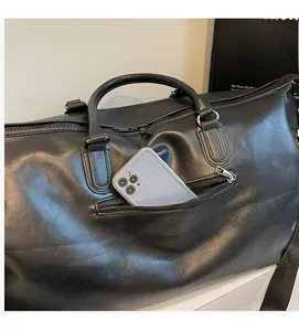 Close-up of the side zipper pocket on a black leather duffle bag holding a smartphone