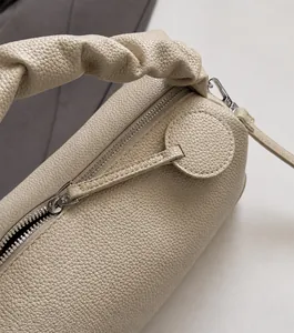 Close-up of litchi texture leather Boston bag featuring a designer pleated handle