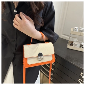 Detailed view of the orange leather trim and silver twist lock on a cream crossbody bag