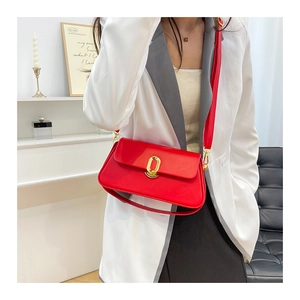 Chic red leather baguette bag with a stylish gold oval clasp worn by a model in a suit