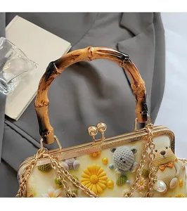 Detail of bamboo handle and gold lock on floral embroidered shoulder bag with pearl charm