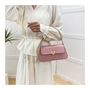 Detail view of pink leather handbag with gold oval buckle held by a model on white background
