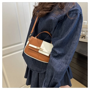 Detail of a two-tone crossbody bag featuring a metal turn-lock closure and leather texture