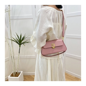 Detail of pink leather crossbody bag with golden oval buckle worn by a female model