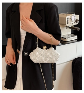 Detail of white lace evening bag featuring a pearl clasp and golden handle on a model