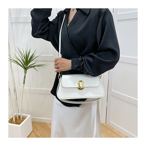 Minimalist white leather bag with golden oval lock shown in a bright interior setting