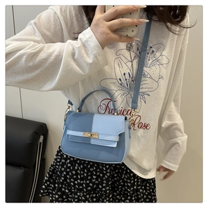 Detail of two-tone blue crossbody bag with gold-tone twist lock buckle on a model