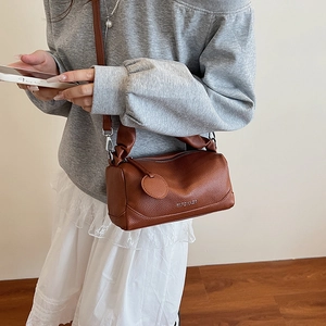 Brown lychee leather Boston bag with top handles and shoulder strap shown on a model
