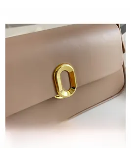 Close-up of elegant oval gold hardware clasp on a beige leather crossbody bag