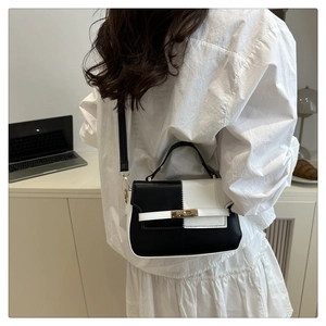 Detail of a two-tone black and white Kelly style handbag with golden twist lock hardware
