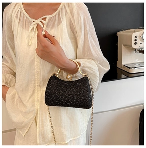Close-up of black sequin evening bag with gold handle, pearl clasp and chain strap
