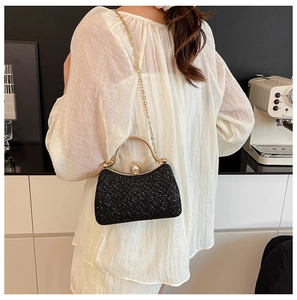 Detail of elegant black sequin evening clutch with gold handle and pearl clasp on model