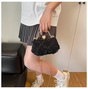 Detail of black lace rose evening bag with gold handle and pearl clasp on metal chain