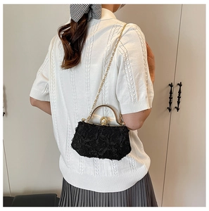 Detailed view of a black lace evening clutch bag with golden chain and pearl clasp on model