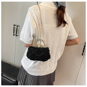 Close-up of black lace evening bag with floral details, gold frame and pearl clasp
