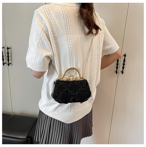 Detail of black lace evening bag featuring a large pearl clasp and gold chain strap