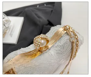Close-up of white lace evening bag with a large pearl clasp and gold snake chain strap