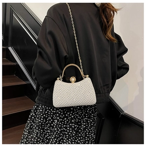 Detailed view of an elegant white woven evening bag with gold handle and chain strap