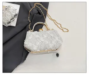 Detail of white lace evening bag with 3D floral textures and gold metal handle ring