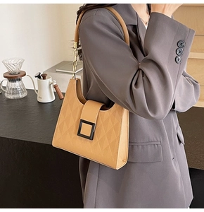 Detail of light brown quilted bucket bag featuring a matte black square buckle and chain strap