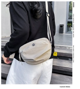 Close-up of beige pleated nylon crossbody bag with adjustable wide strap and metal logo