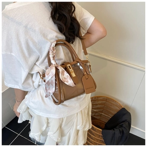 Detailed view of brown PVC bucket bag with silk scarf handle and golden twist lock