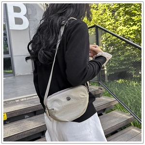 Detailed side view of the beige crescent nylon shoulder bag worn by a model