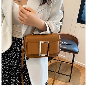 Close-up of caramel leather crossbody bag featuring a large gold buckle and slim strap